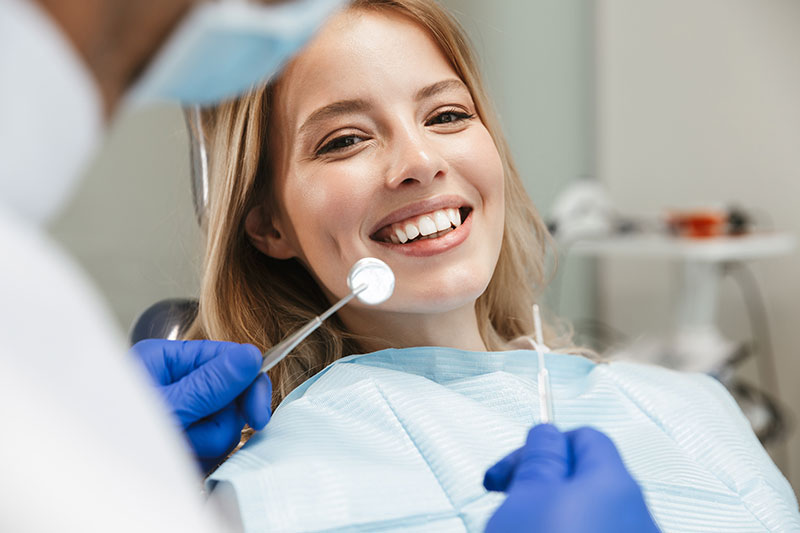satisfied woman sitting in dental chair while professional dentist looks at her teeth